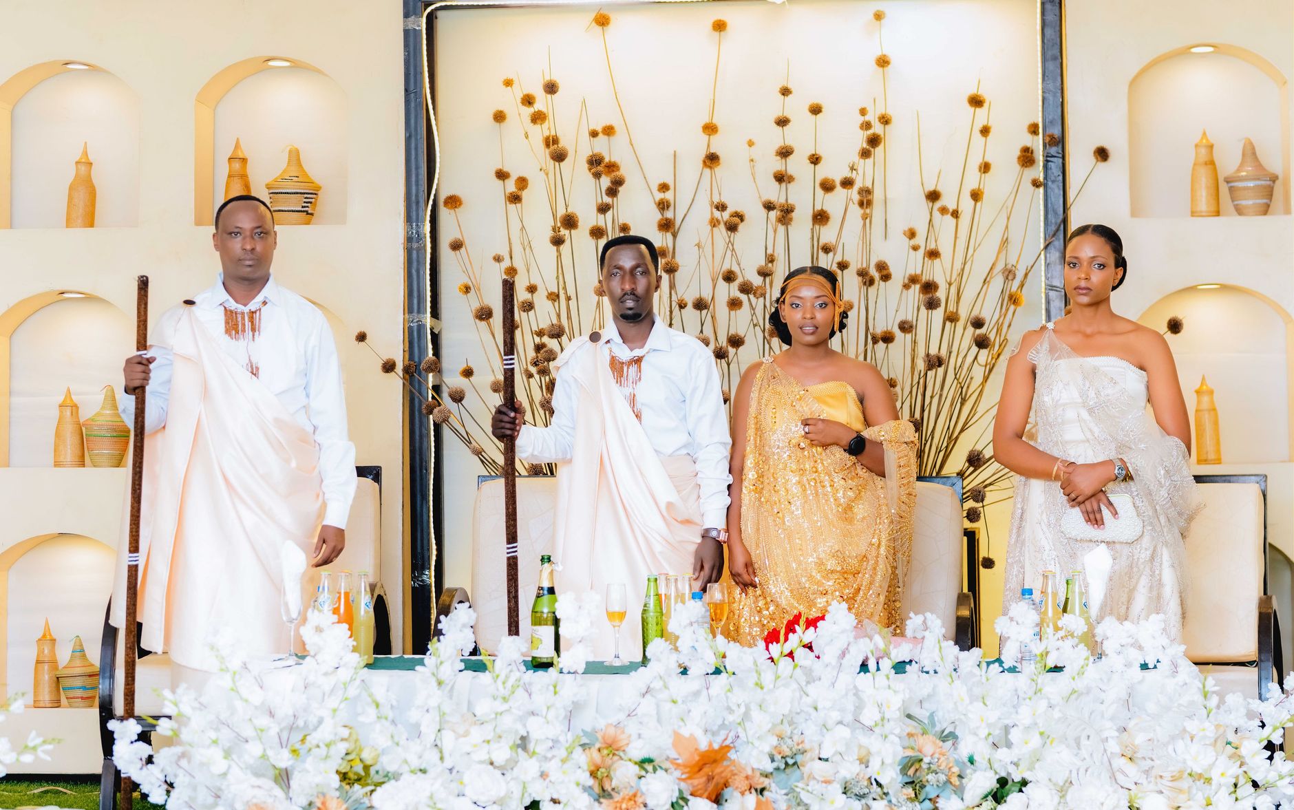 Group of adults in elegant traditional African attire posing indoors at a wedding ceremony.