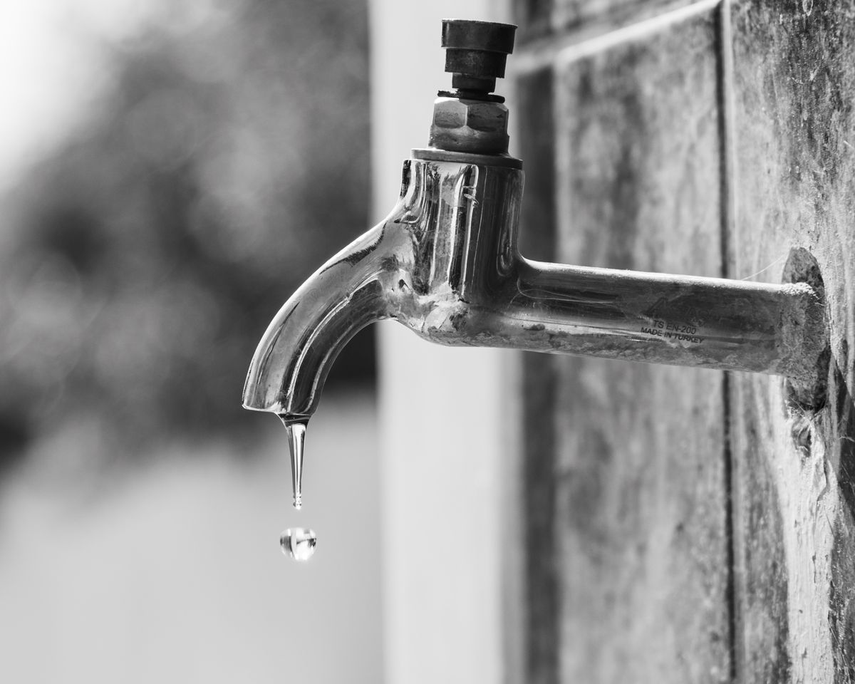 Black and white photo of a dripping outdoor faucet.