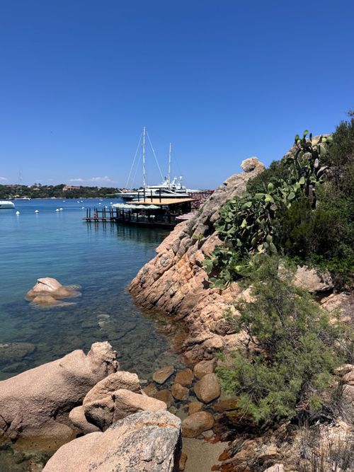 Free Serene view of sailboats and rocky shore in Sardinia, Italy under clear blue skies. Stock Photo