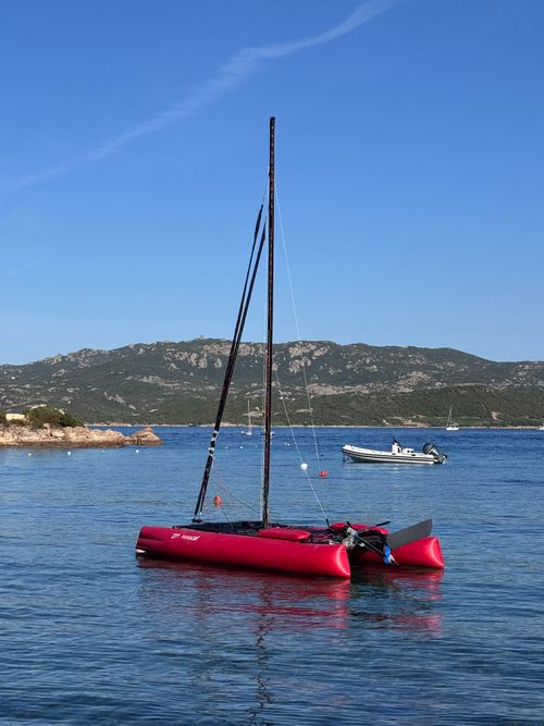 Free Red catamaran sailing in clear waters of Sardinia, Italy with mountainous backdrop. Stock Photo