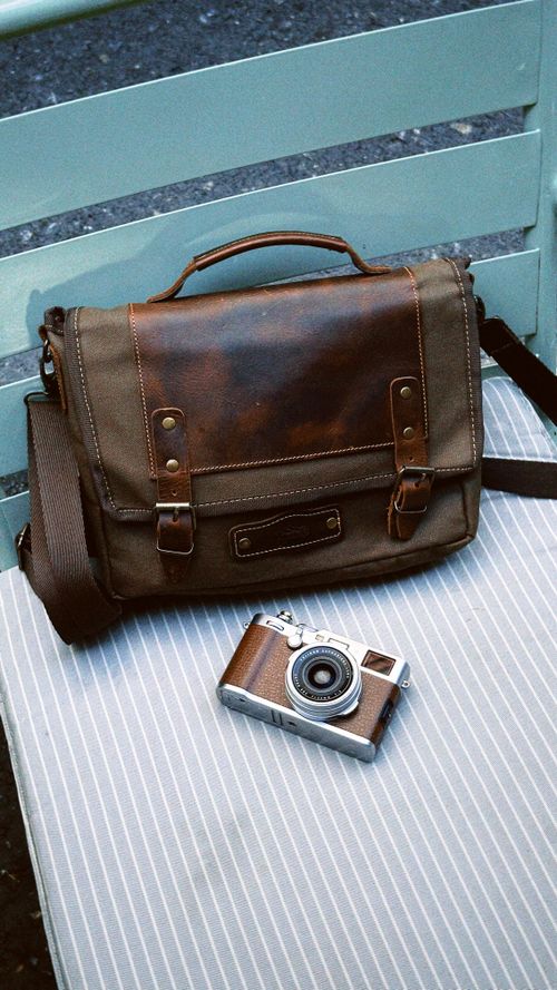 Free A classic brown leather bag and retro camera on a striped chair create a nostalgic scene. Stock Photo