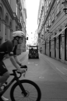 A cyclist rides through a historic street in Vienna, capturing motion and architecture in black and white.