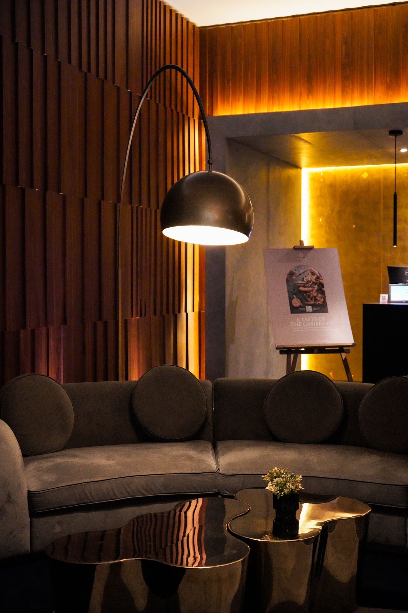 Warm lounge with curved velvet seating, a brass arc lamp and timber slat walls