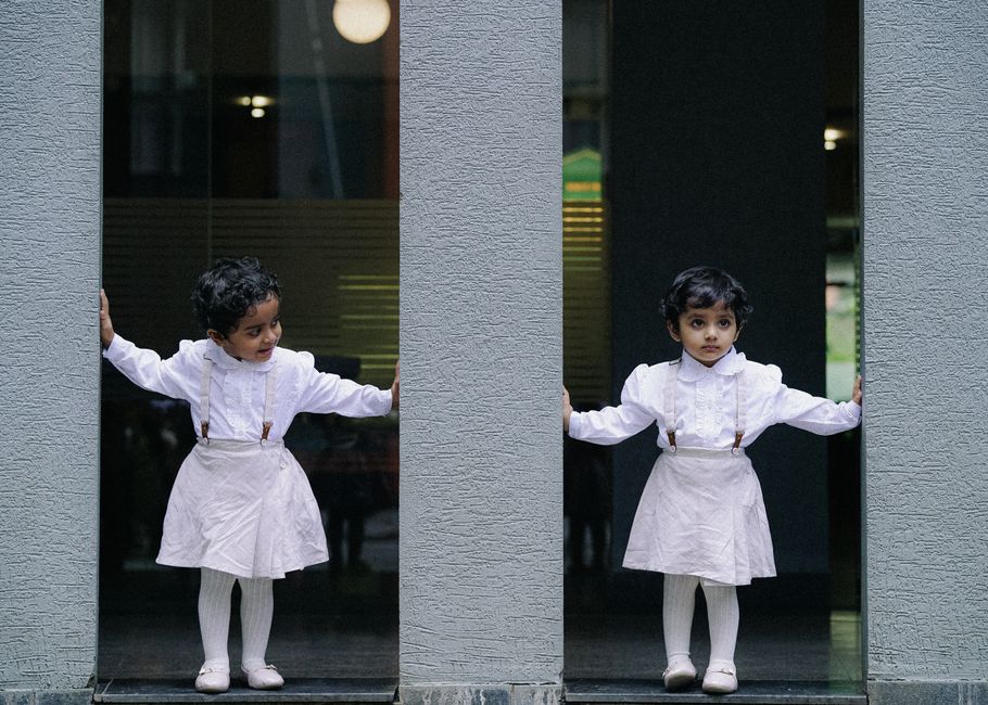 Charming portrait of twin girls in matching white dresses posing playfully in an urban setting.