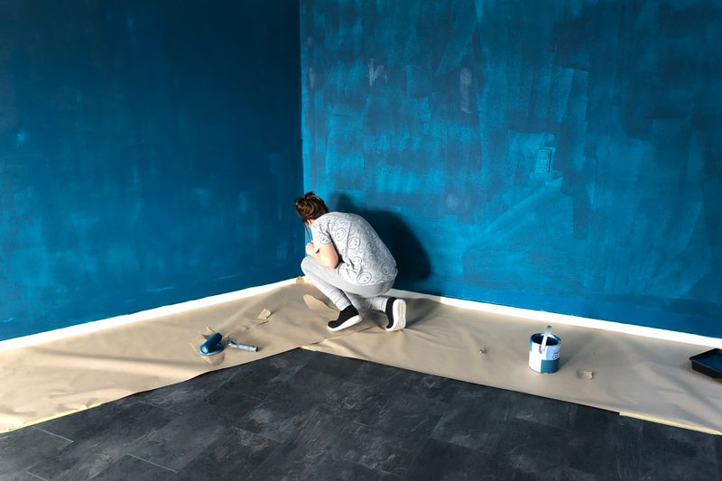 A woman painting a blue wall indoors for a home renovation project.