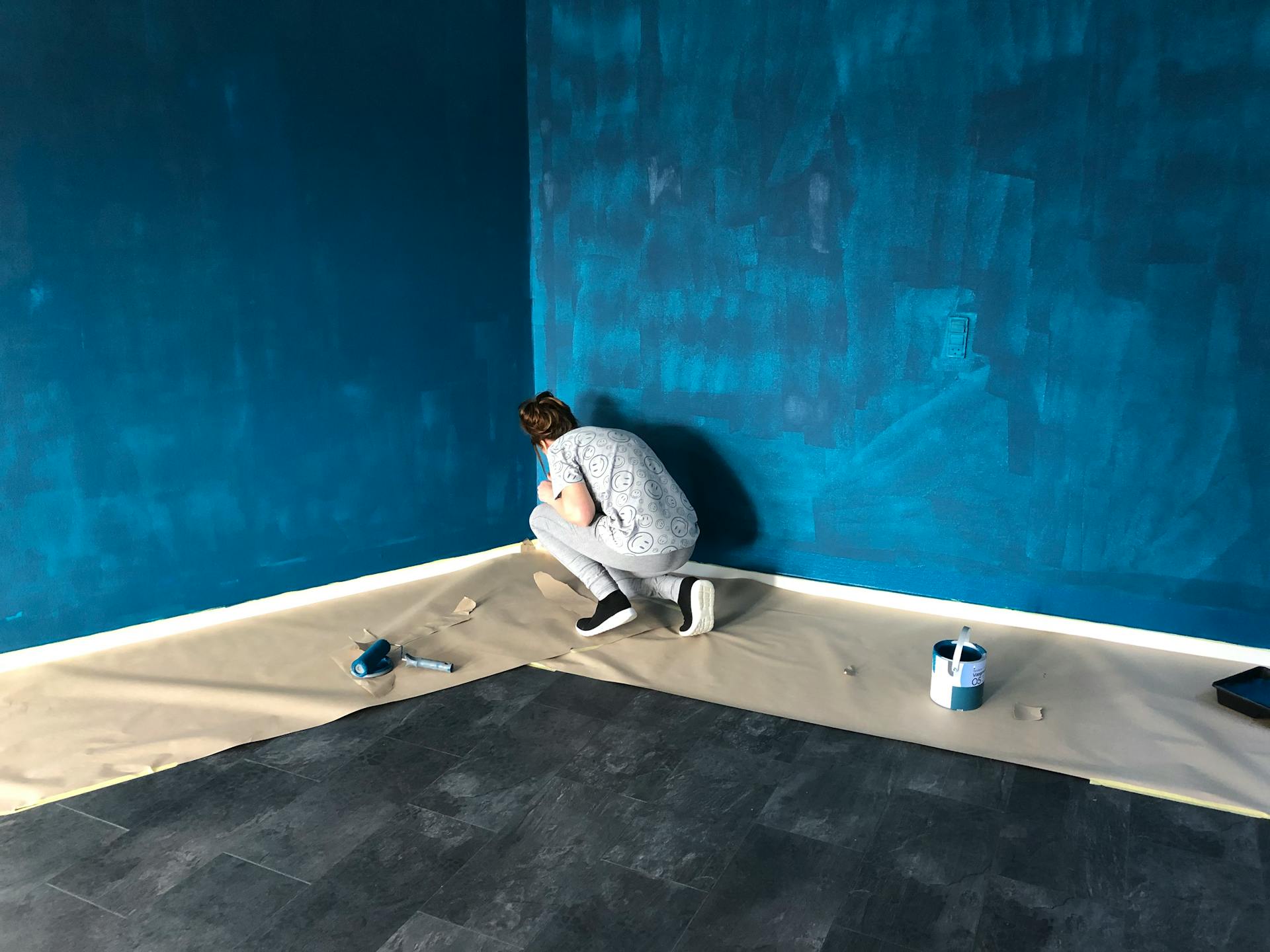 A woman painting a blue wall indoors for a home renovation project.