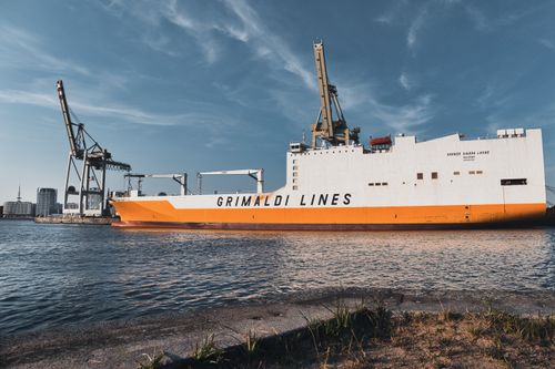 Free Grimaldi Lines cargo ship docked at a port with cranes on a sunny day, showcasing maritime industry. Stock Photo