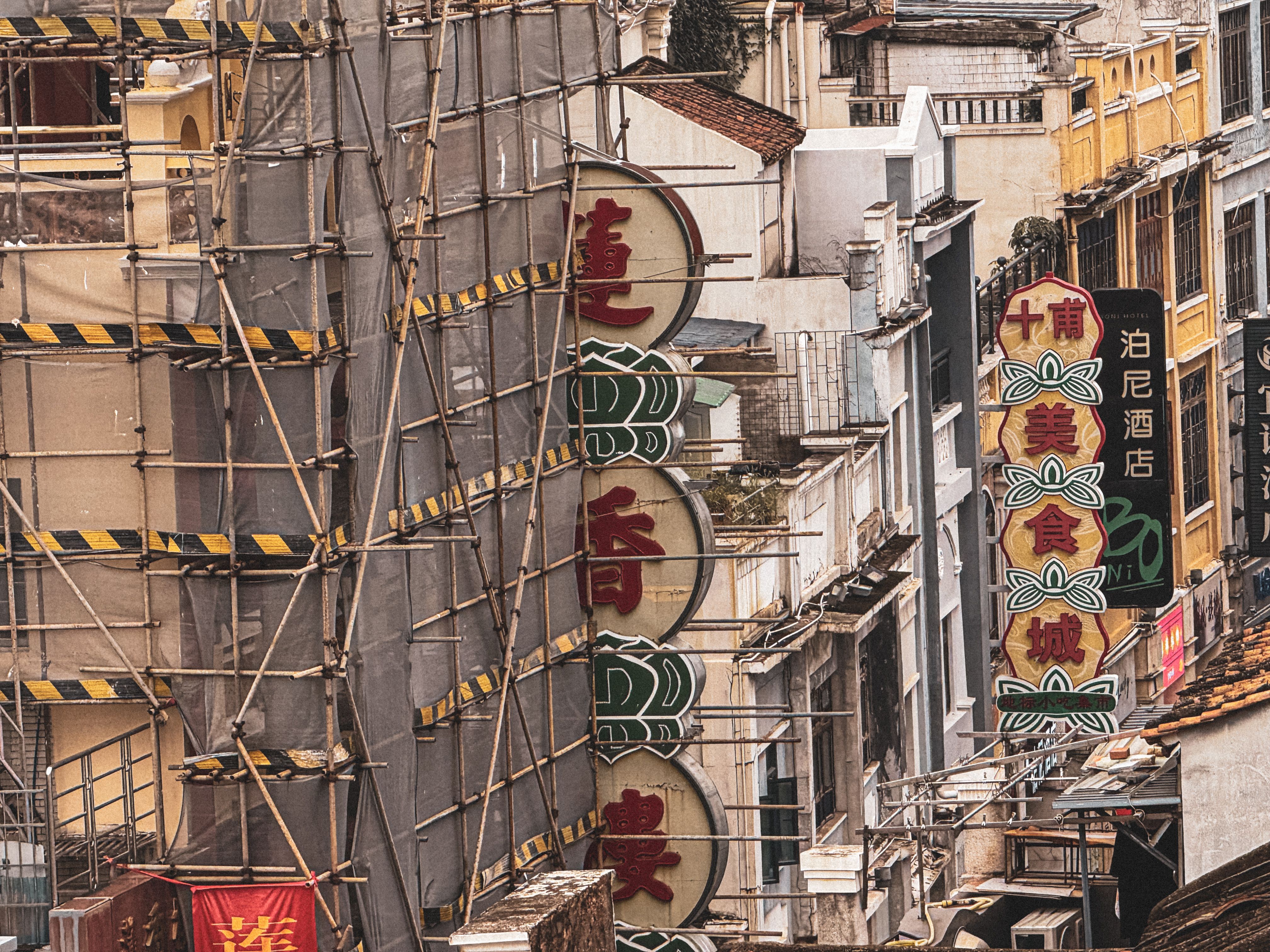 A bustling city street lined with neon signs and scaffolding, depicting urban development and vibrant culture.