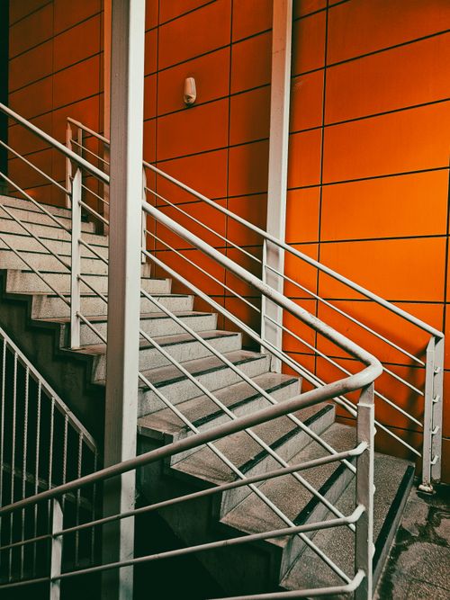 Free A sleek indoor staircase with orange-paneled walls and metal railings. Stock Photo