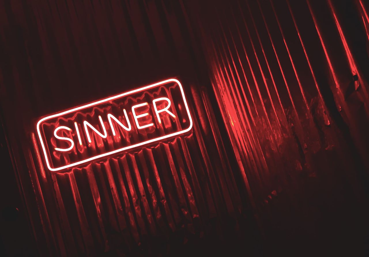 bright red neon sign displaying the word sinner against a dark moody b