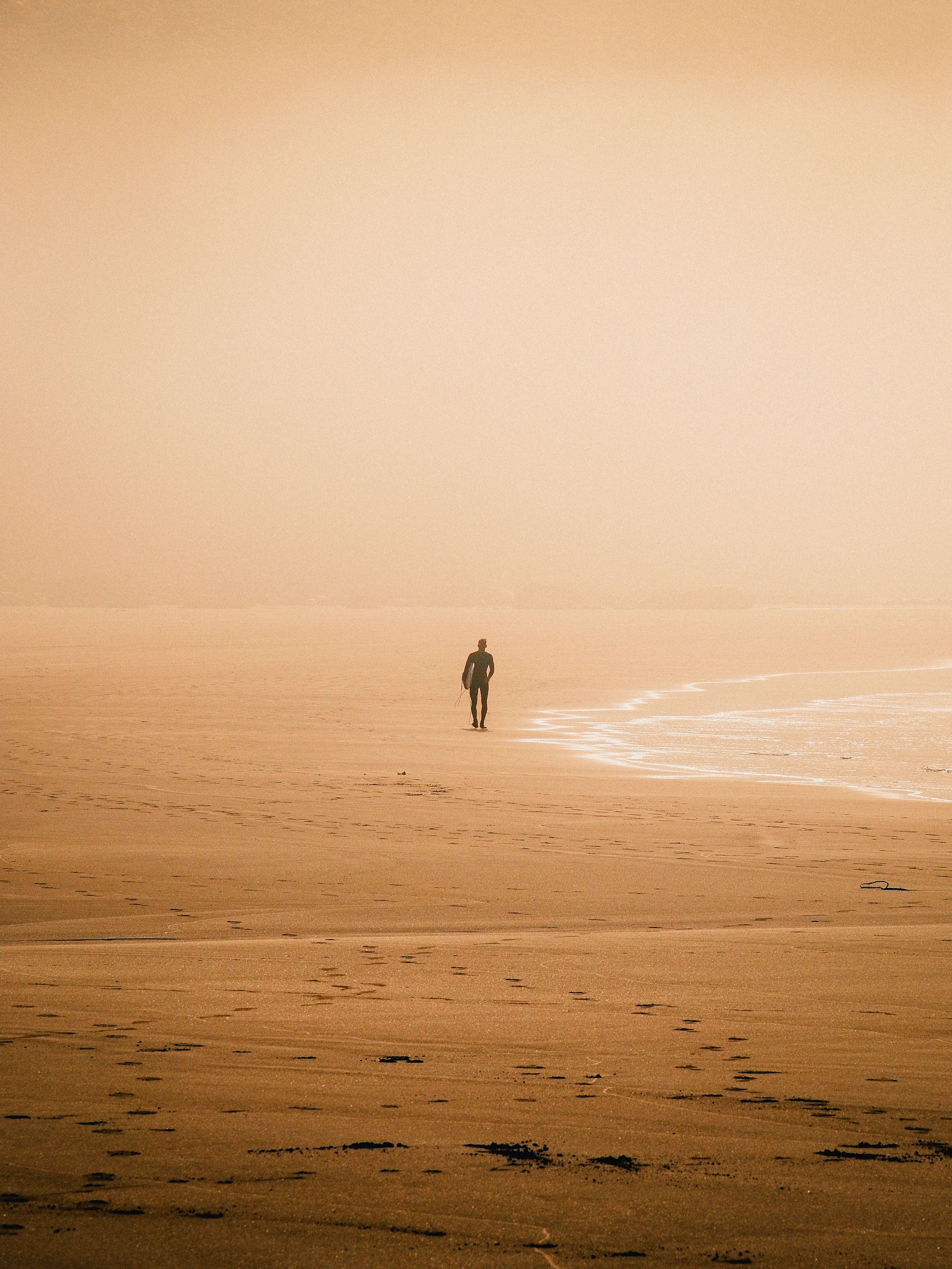 A lone person strolls along a misty beach at sunset, evoking solitude.