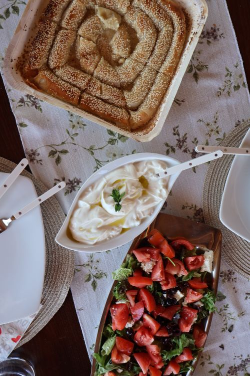 Free Top-down view of a traditional Greek meal featuring salad, yogurt, and baked bread on a decorative table. Stock Photo
