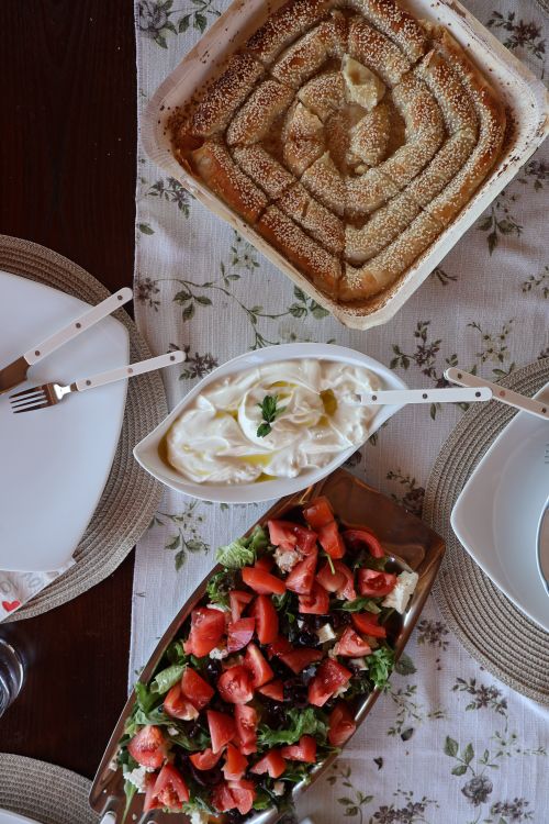 Free Delight in a delicious Greek meal featuring a savory pie, fresh Mediterranean salad, and creamy yogurt dip. Stock Photo