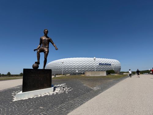 Free Statue of Franz Beckenbauer with Allianz Arena in Munich, Germany under a clear blue sky. Stock Photo