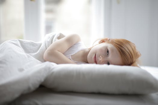 A redhead girl lying comfortably on a white bed, enjoying a peaceful rest.