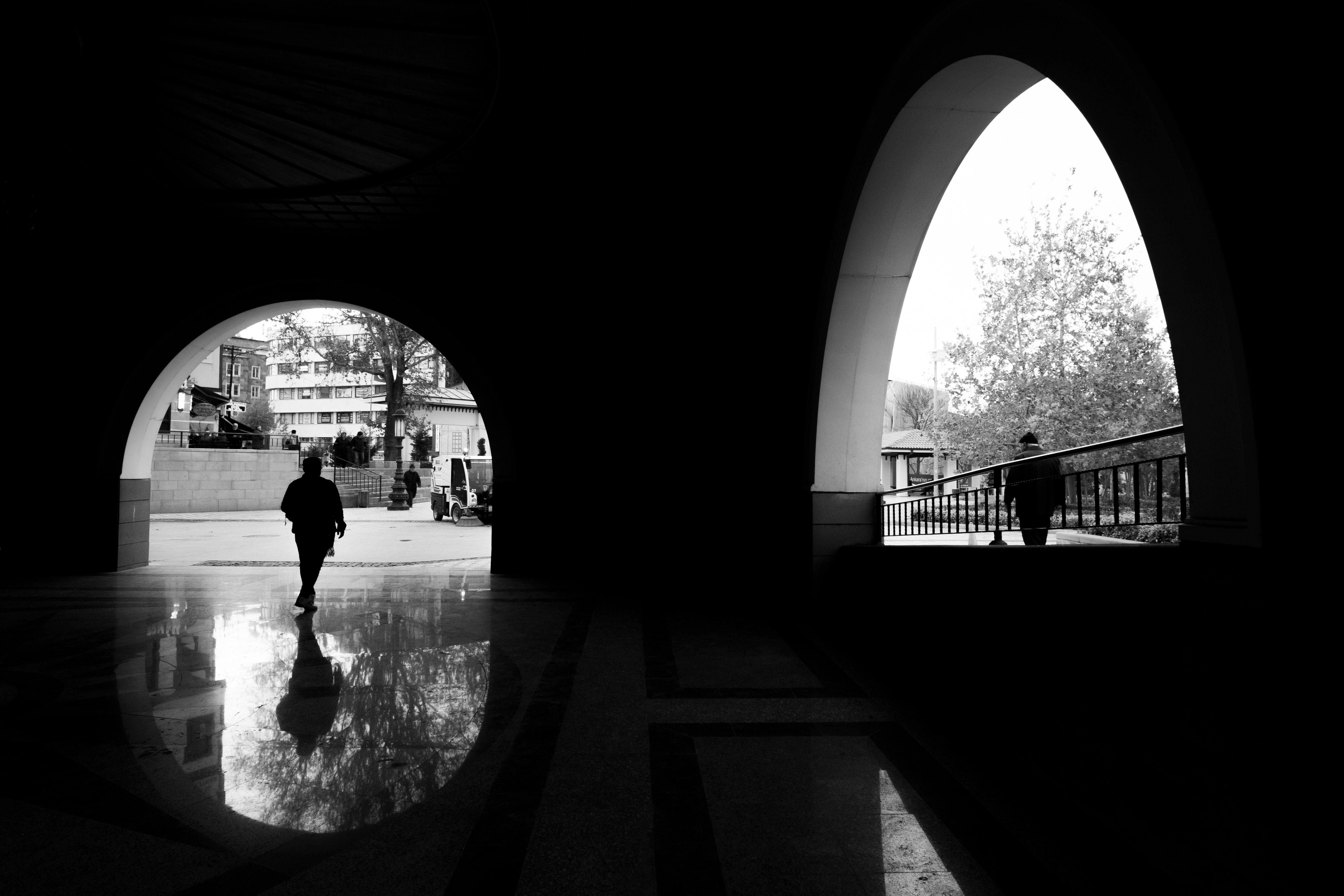 Black and white image of silhouetted figures walking through an archway in a city setting.