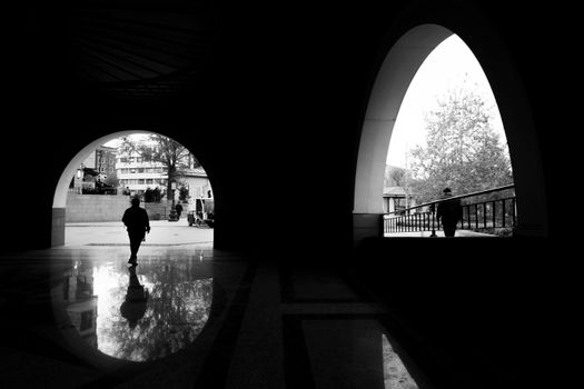 Black and white image of silhouetted figures walking through an archway in a city setting.