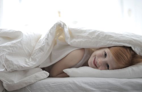 Free Young girl smiling under a blanket, enjoying a cozy and calm indoor atmosphere. Stock Photo