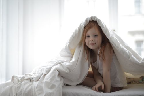 Free A joyful child playing under a white blanket in a bright and cozy bedroom. Stock Photo