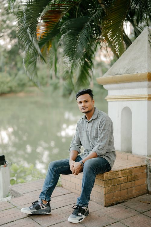 Free A young man sitting casually by a serene lake surrounded by greenery. Stock Photo