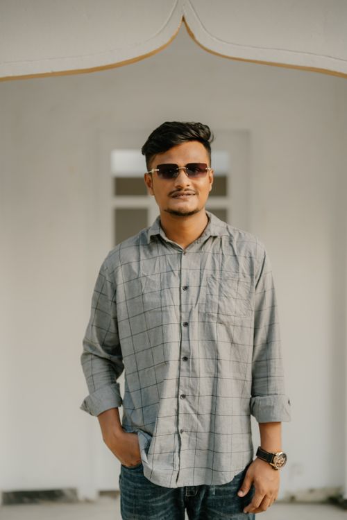 Free A young man in sunglasses and a casual shirt stands confidently indoors, exuding a relaxed vibe. Stock Photo
