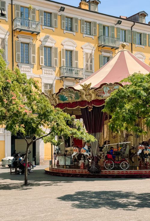 Free Sunlit carousel in Nice, France surrounded by historic buildings and greenery. Stock Photo