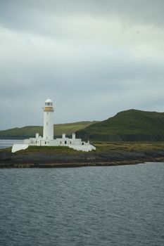 Scenic view of the Isle of Mull lighthouse overlooking calm waters and rolling hills at dusk.