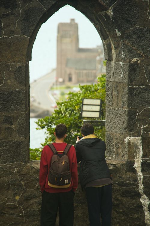Free Two individuals admire a scenic view through a historic stone archway, capturing a moment of exploration. Stock Photo