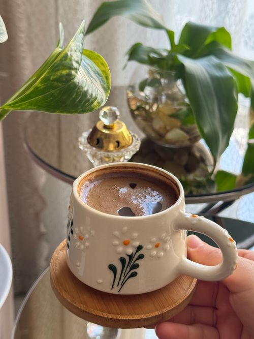 Free A cozy coffee moment indoors with a decorated mug amidst lush green plants and soft daylight. Stock Photo
