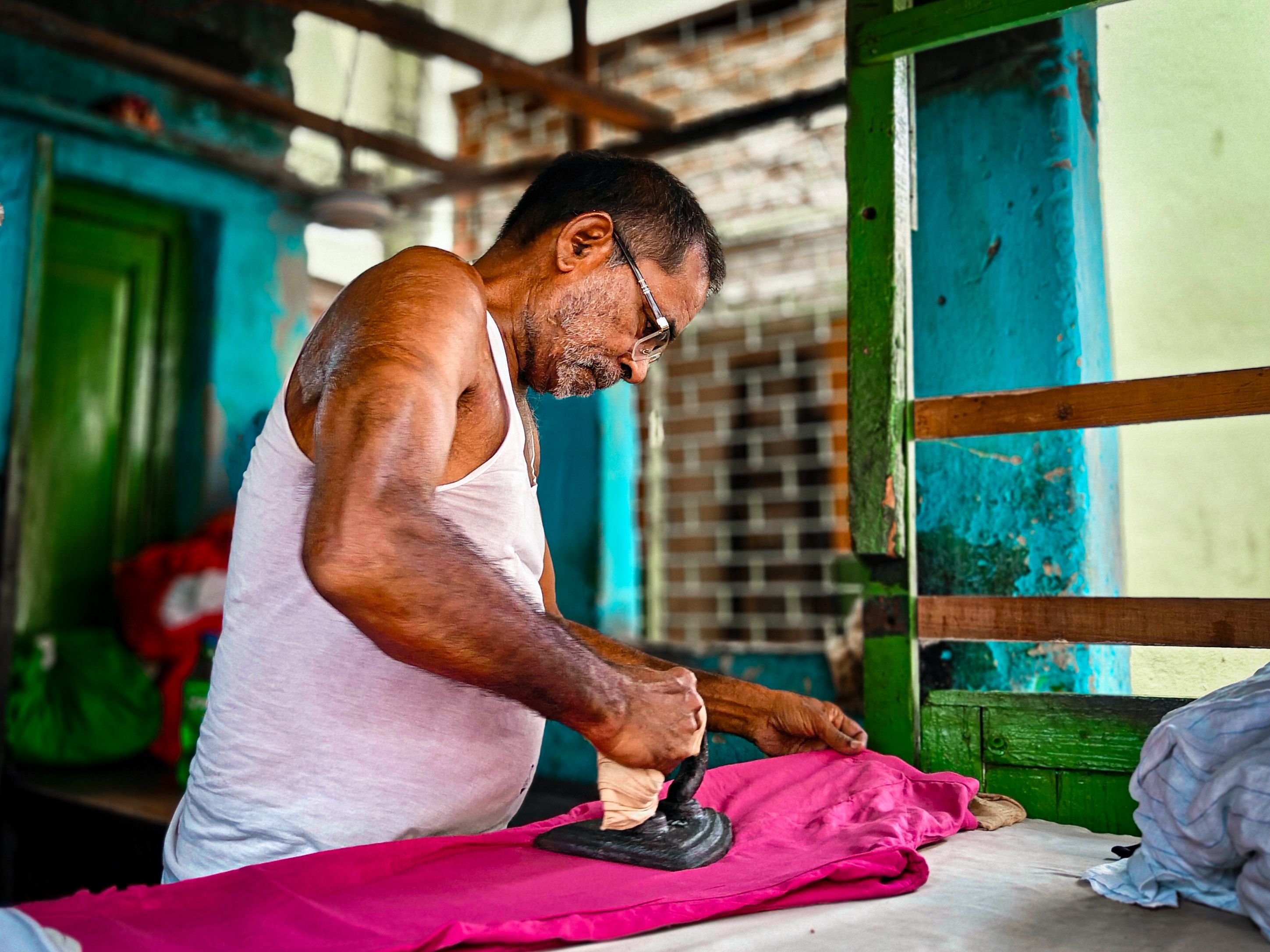 An elderly man diligently ironing clothes in a vibrant, rustic indoor setting.