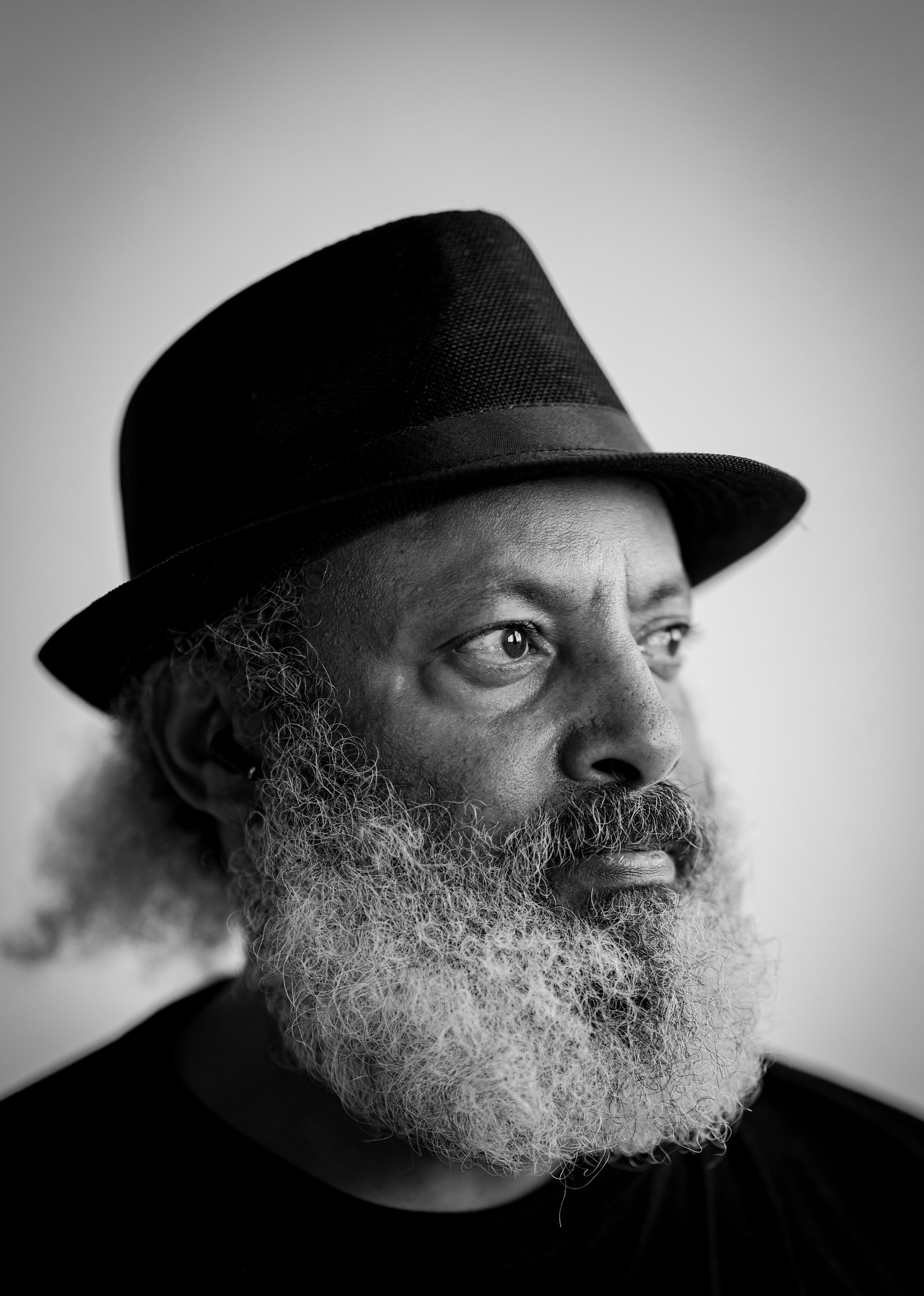 Black and white portrait of an elderly man with a beard in a black hat gazing thoughtfully.