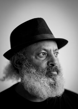 Black and white portrait of an elderly man with a beard in a black hat gazing thoughtfully.