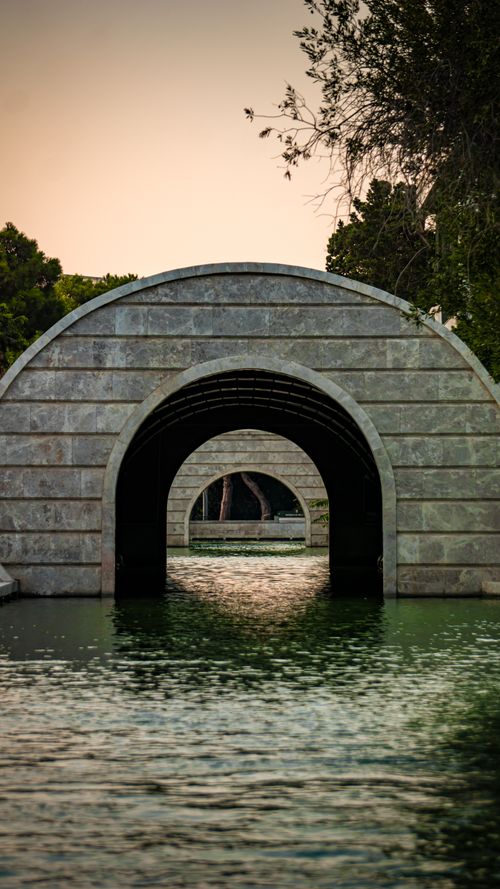 Free Stone archway reflecting on calm water at sunset, evoking symmetry and tranquility. Stock Photo