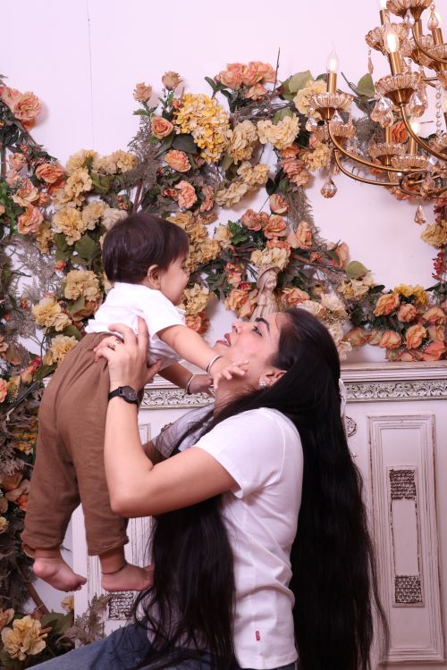 Free Joyful moment of a mother lifting her child, surrounded by floral decor indoors. Stock Photo
