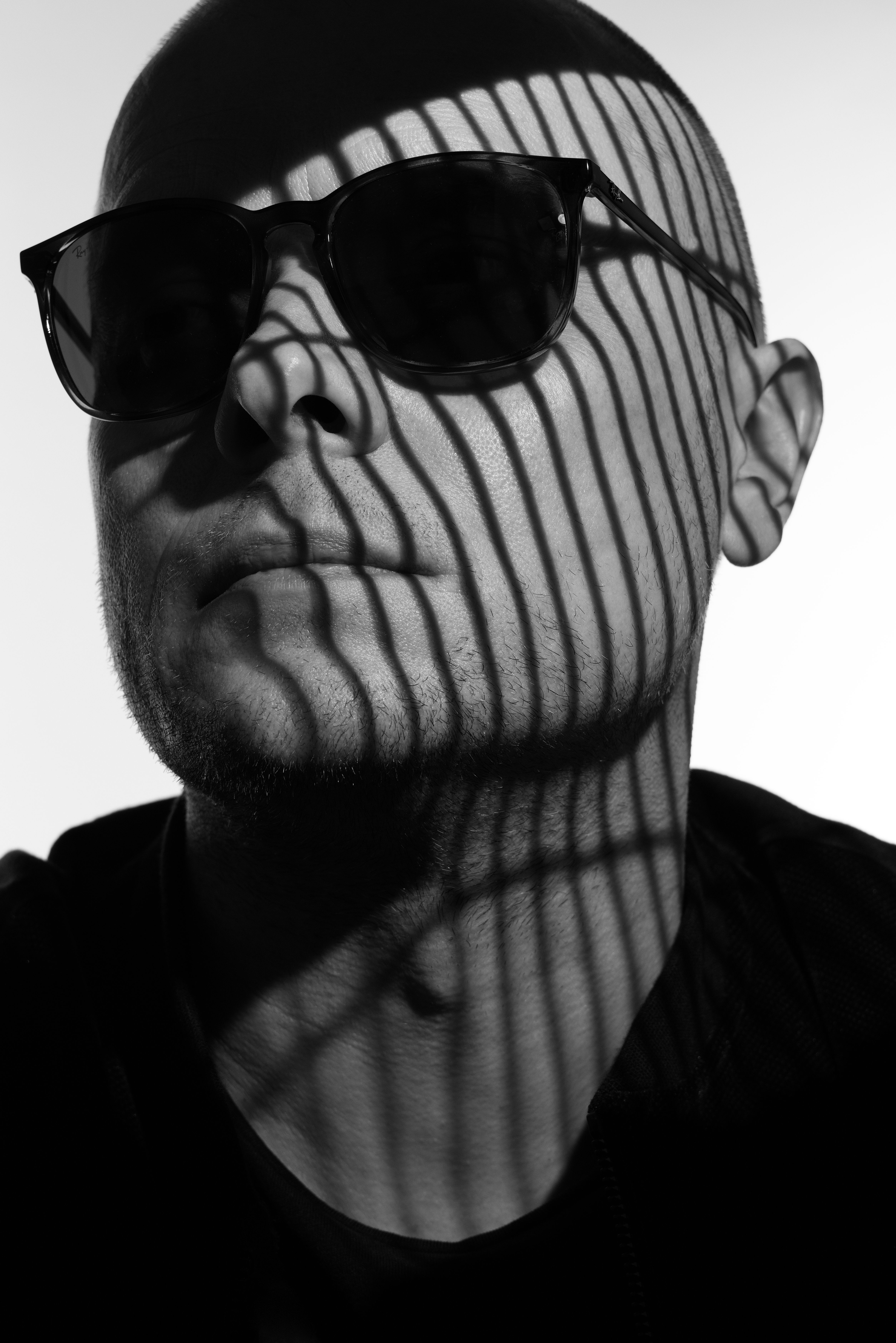 Moody black and white portrait of a man with striped shadows over his face.