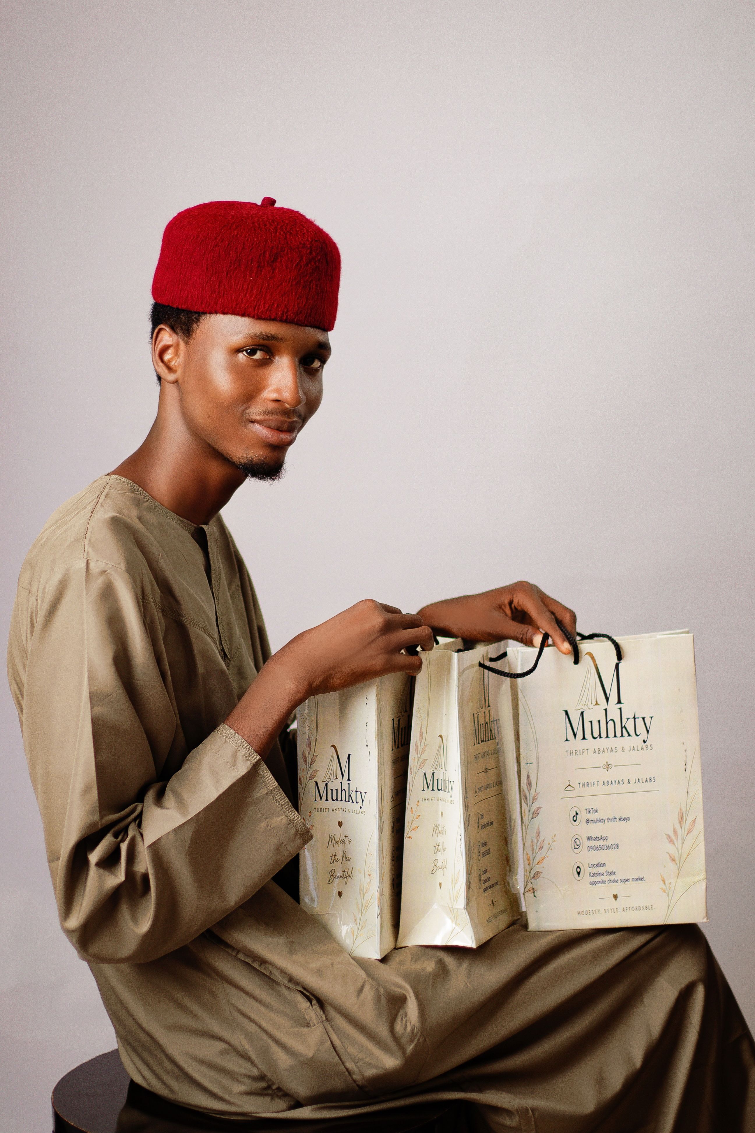 Man wearing cultural dress and holding shopping bags against a plain background.
