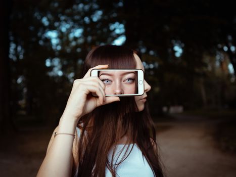 一位女性在户外手持智能手机，眼睛图像覆盖其上，呈现艺术概念
