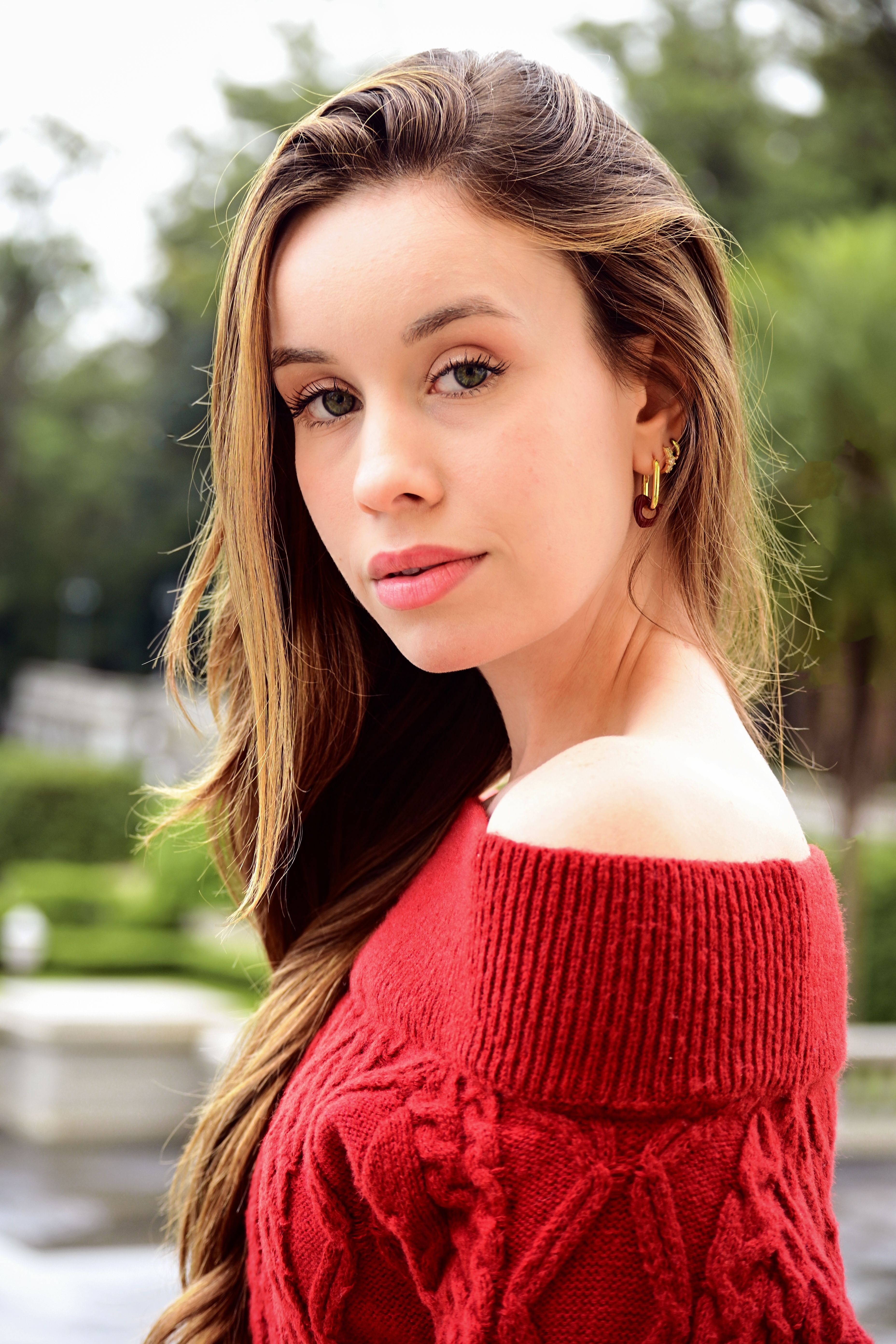 Elegant woman in a red sweater posing outdoors, exuding confidence and style.