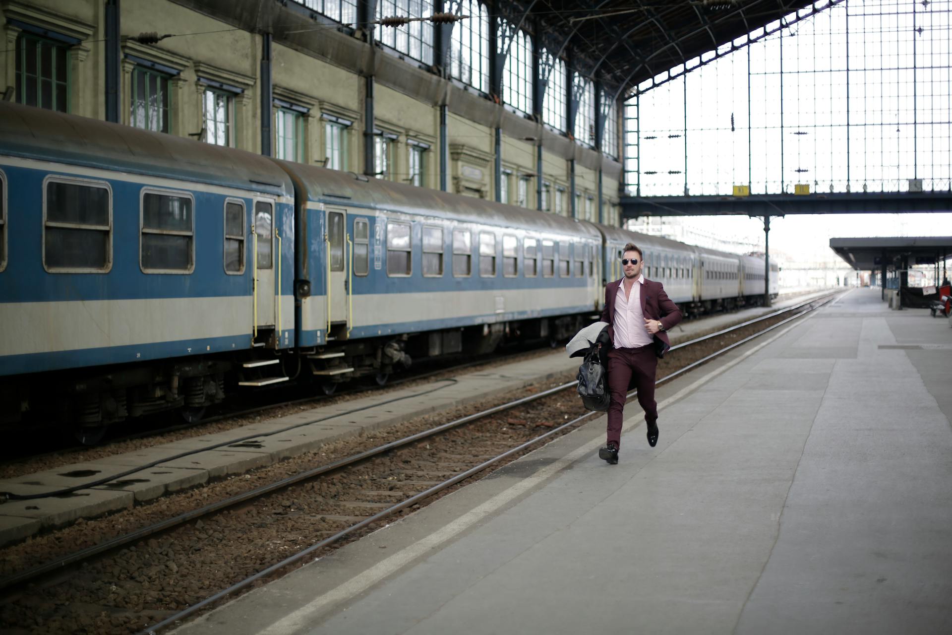 A businessman in a purple suit runs on a railway platform, rushing to catch a train during daylight.