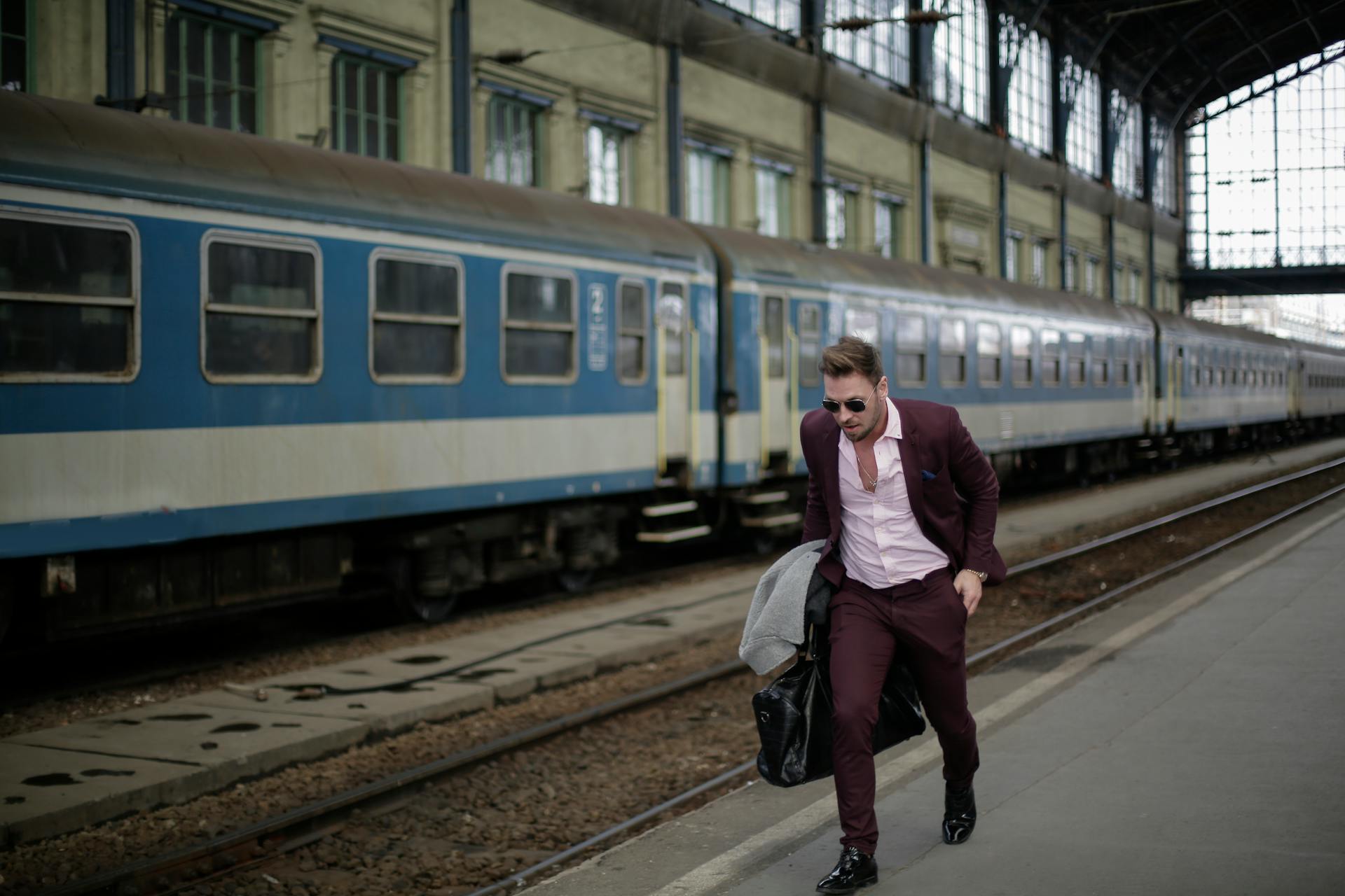 Businessman in suit dashing through railway station beside blue train cars.