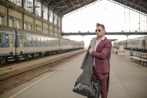 Free Stylish man in maroon suit and sunglasses waiting at a historic railway station. Stock Photo
