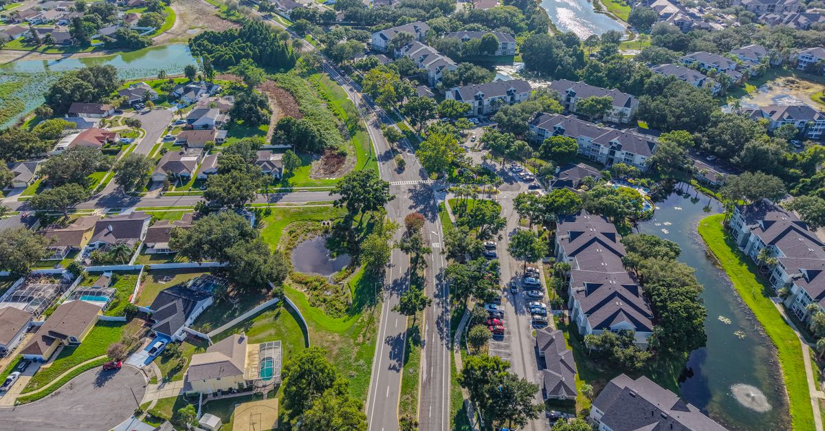 Detailed aerial view of a residential neighborhood in sunny Florida, showcasing houses, roads, and green areas.