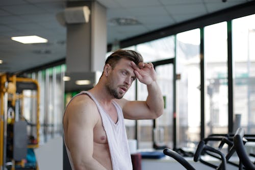 Man in White Tank Top Feeling His Forehead