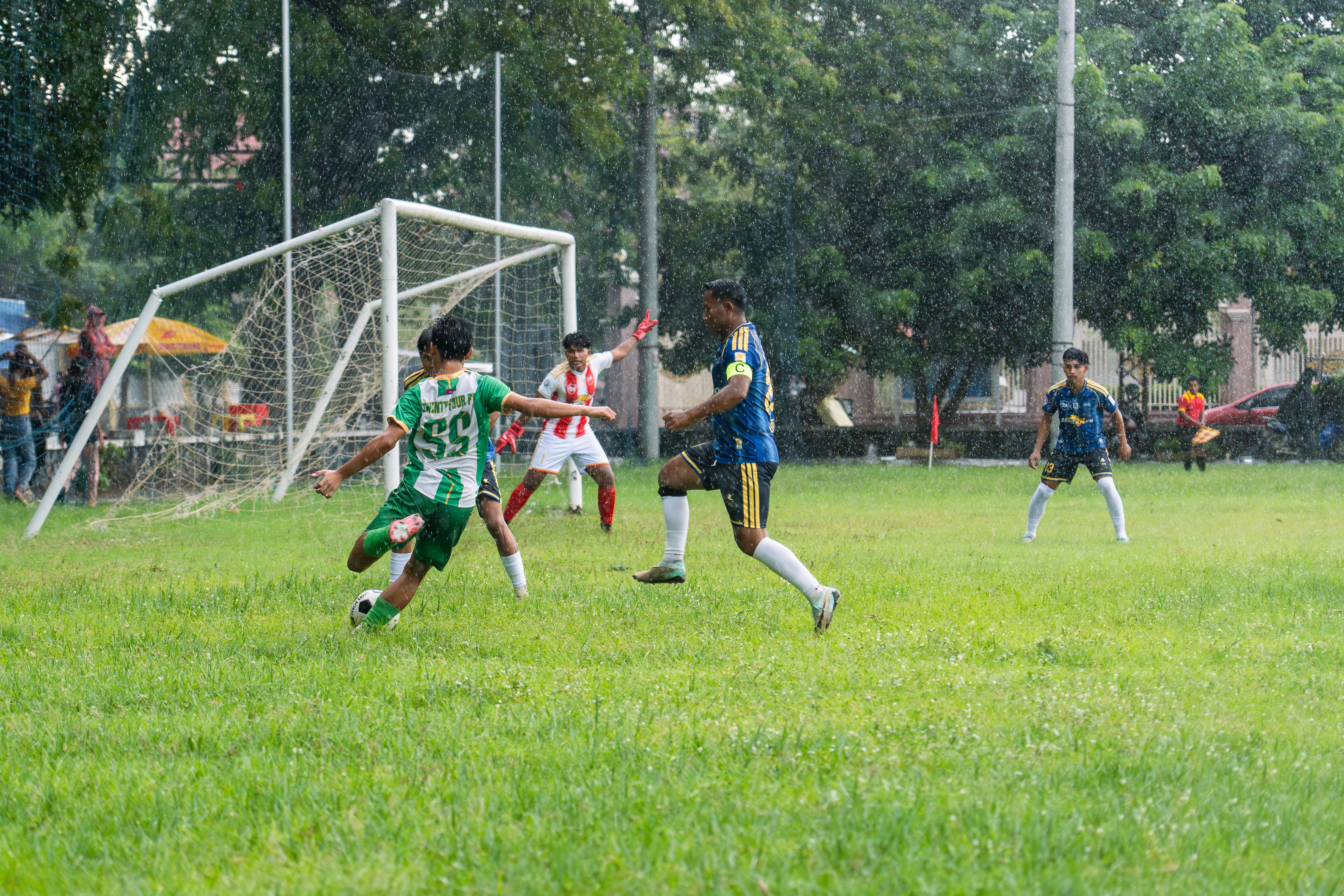 Intense soccer match in the rain with players in action near goalpost on a grassy field.