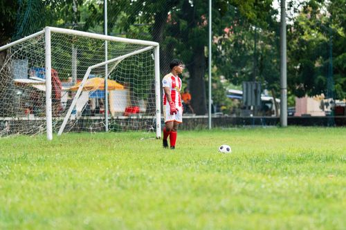 Free Soccer goalkeeper in action on outdoor field. Player in red kit ready near goal. Stock Photo