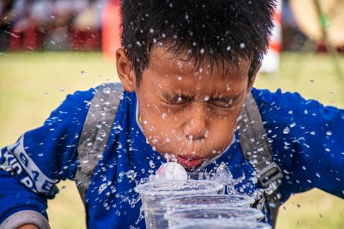 Free A boy concentrating as he plays a water game, splashing water with focus and determination outdoors. Stock Photo