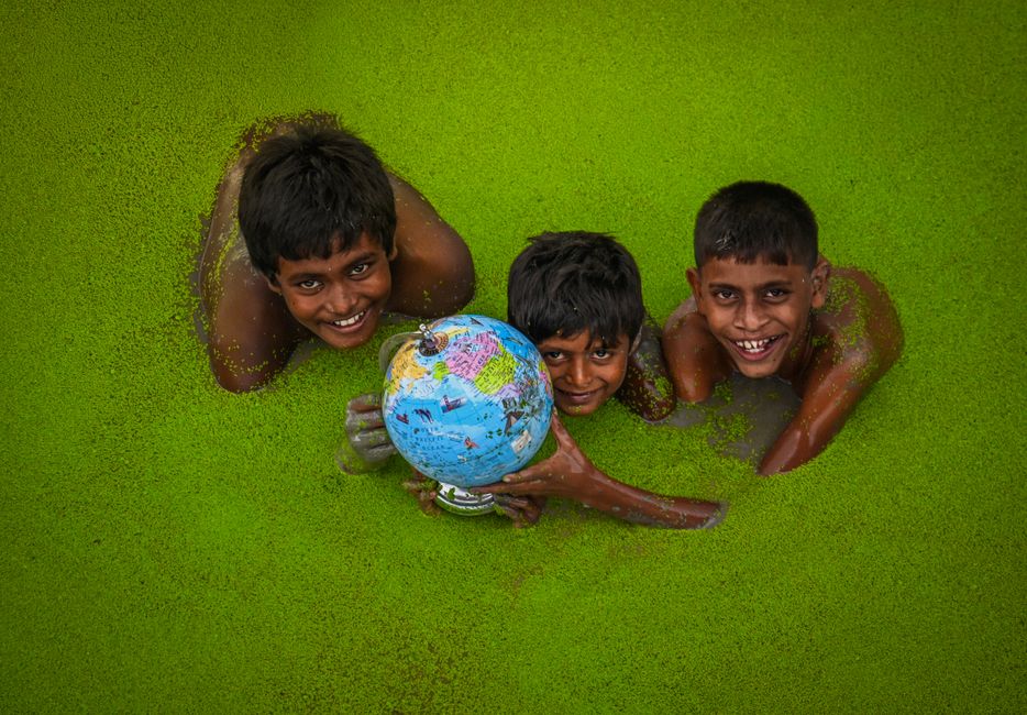 Three children play happily in a green lake in India, holding a globe.