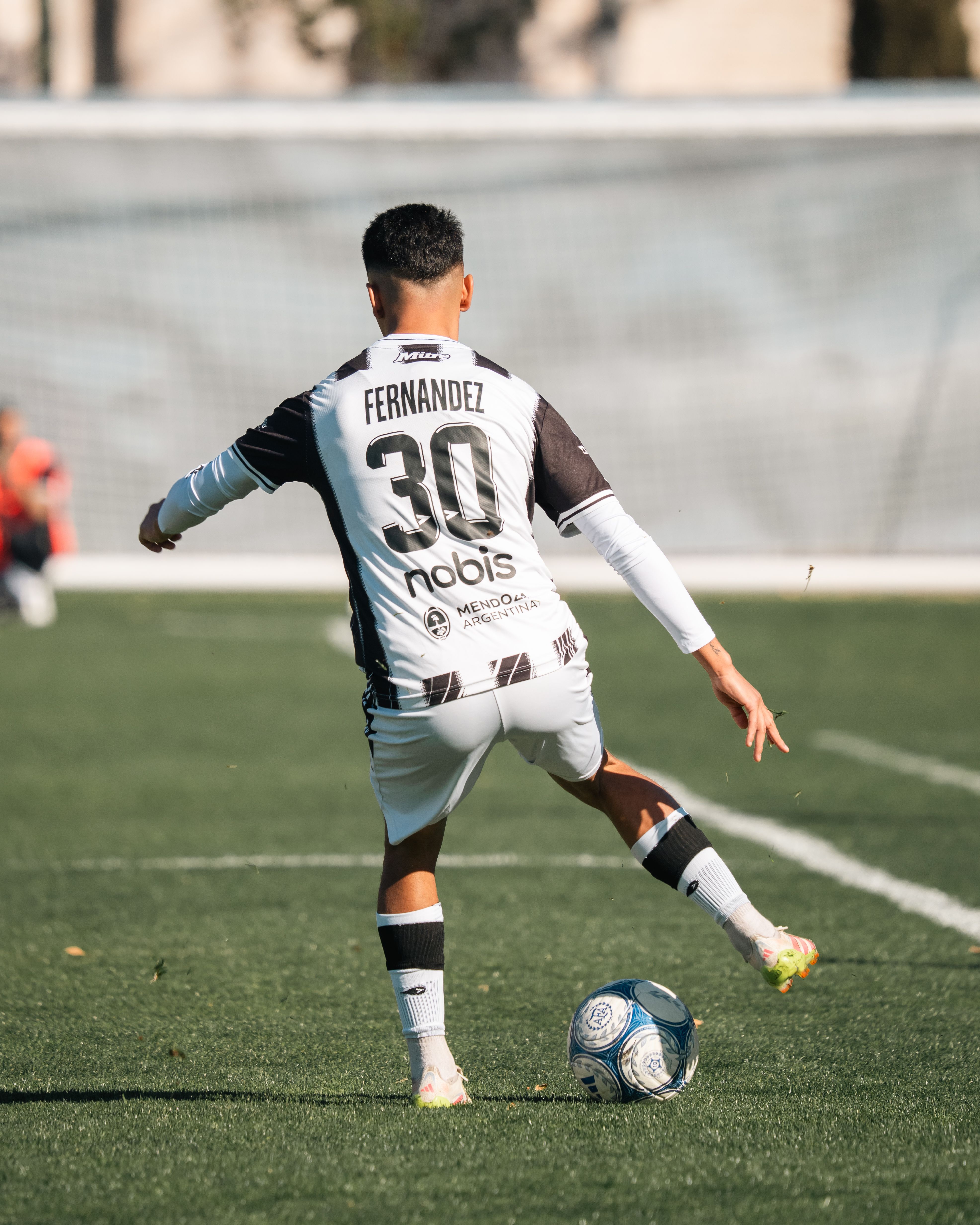 Soccer player in action kicking a ball during a game on a sunny day.