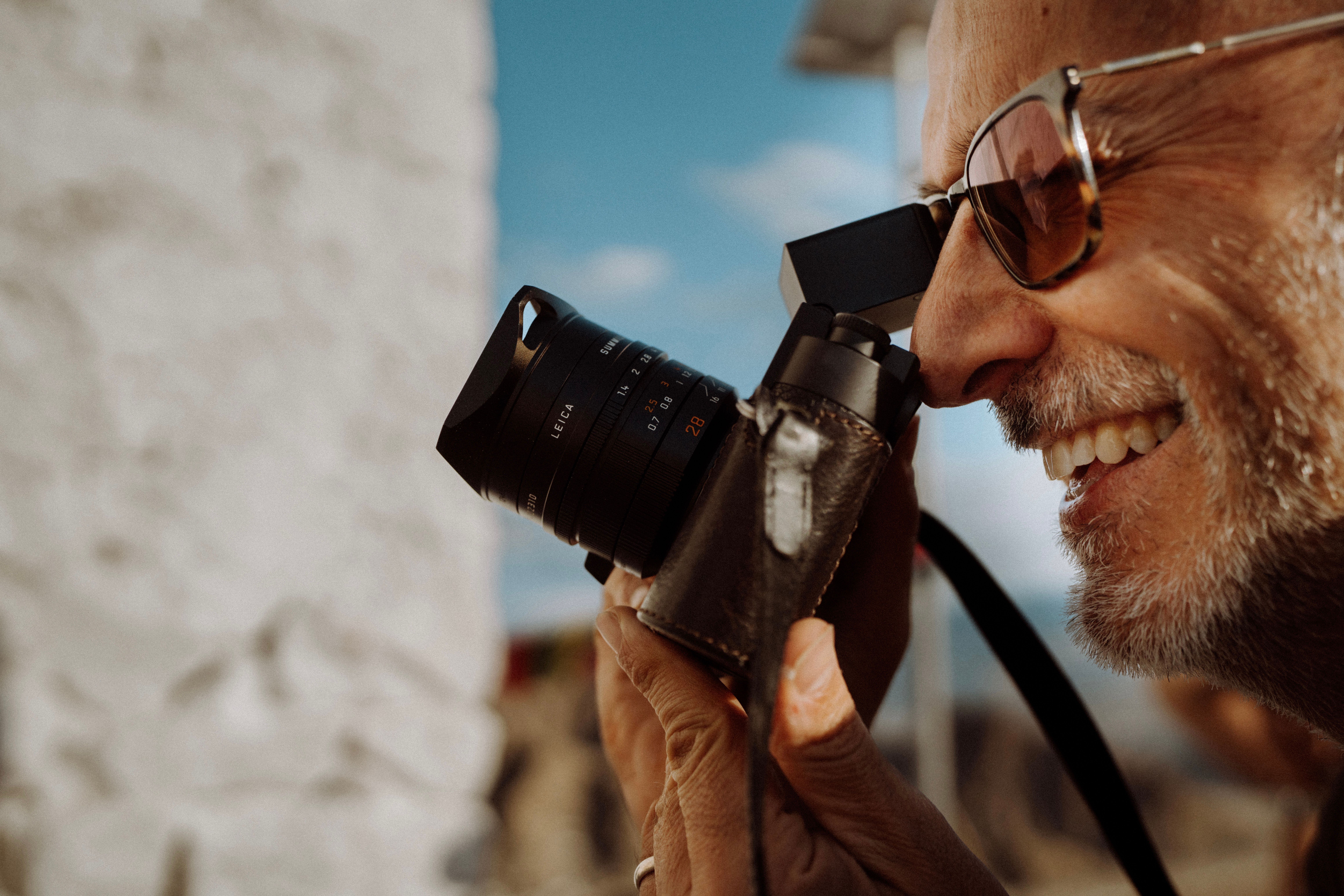 Close-up of a smiling man taking a photo with a vintage camera outdoors.