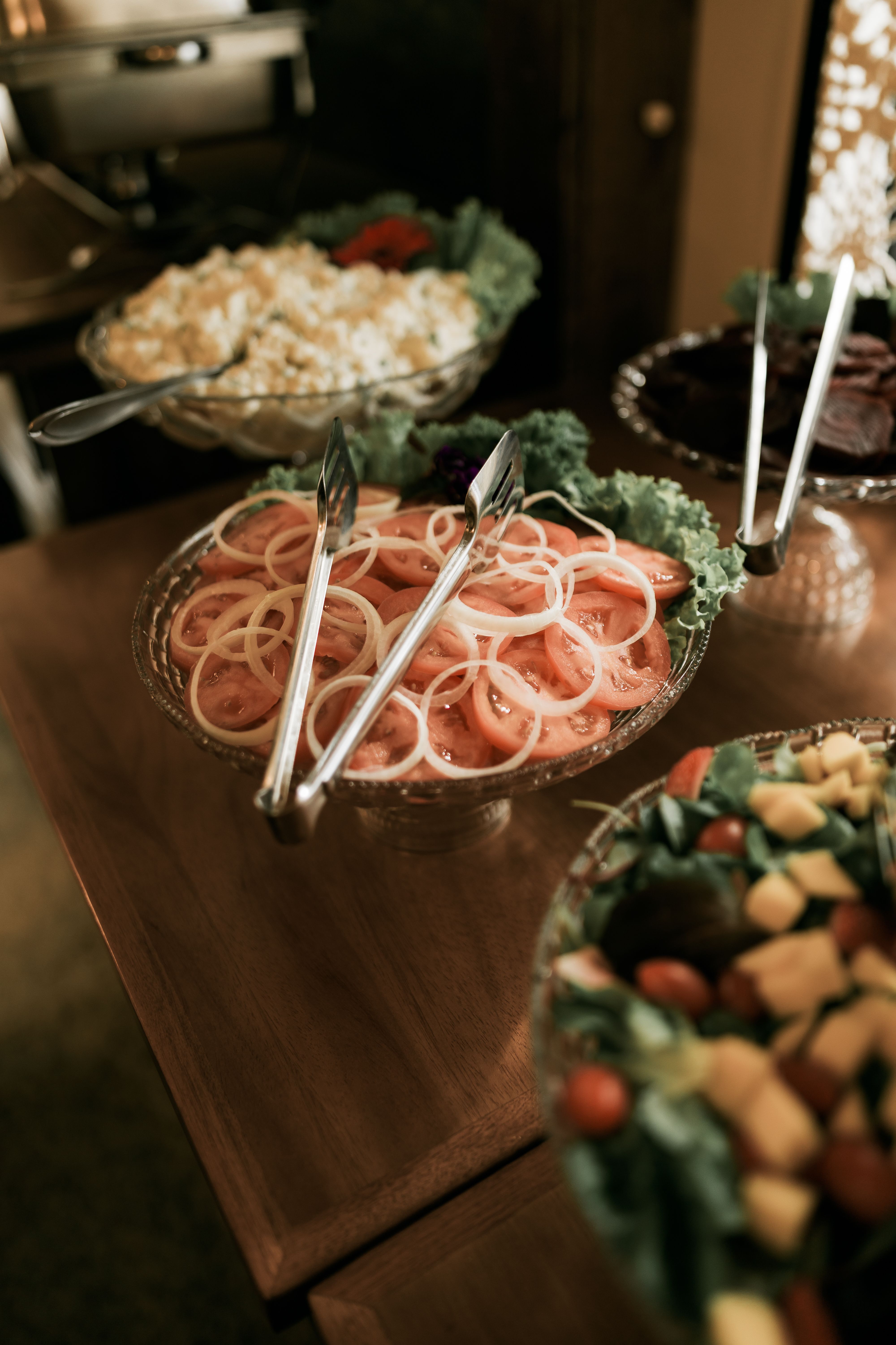 Coupe en verre de tomates et rondelles d'oignon avec pinces de service, dans une enfilade de saladiers sur un buffet froid